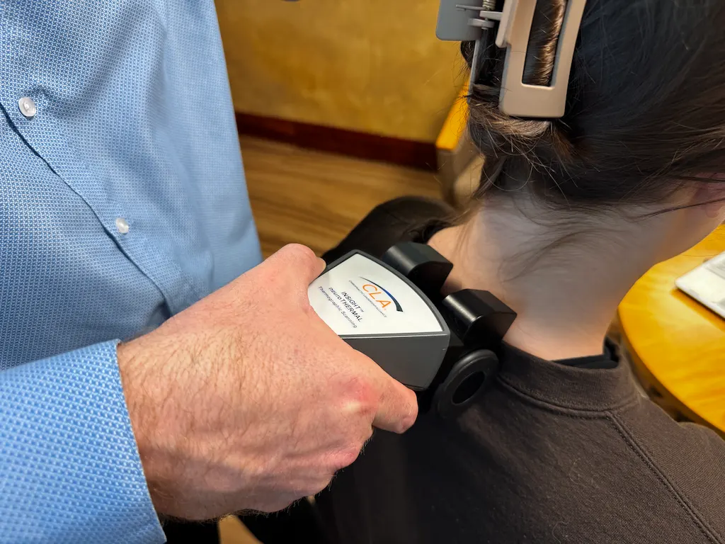 A person's neck and upper back are being scanned by a 'CLA Insight NeuroThermal' device held by another person.