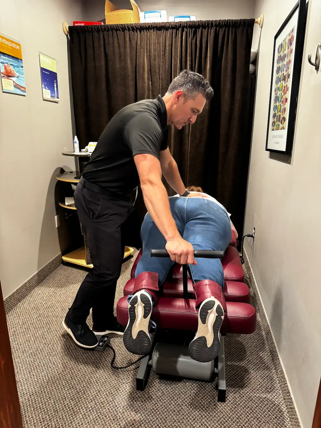 A male chiropractor adjusts a female patient's lower back on a red chiropractic treatment table.