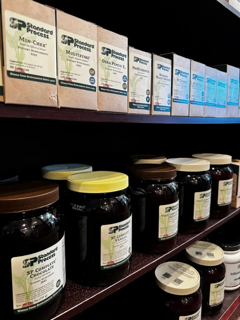 Two shelves filled with various Standard Process dietary supplements in brown boxes and dark glass jars.