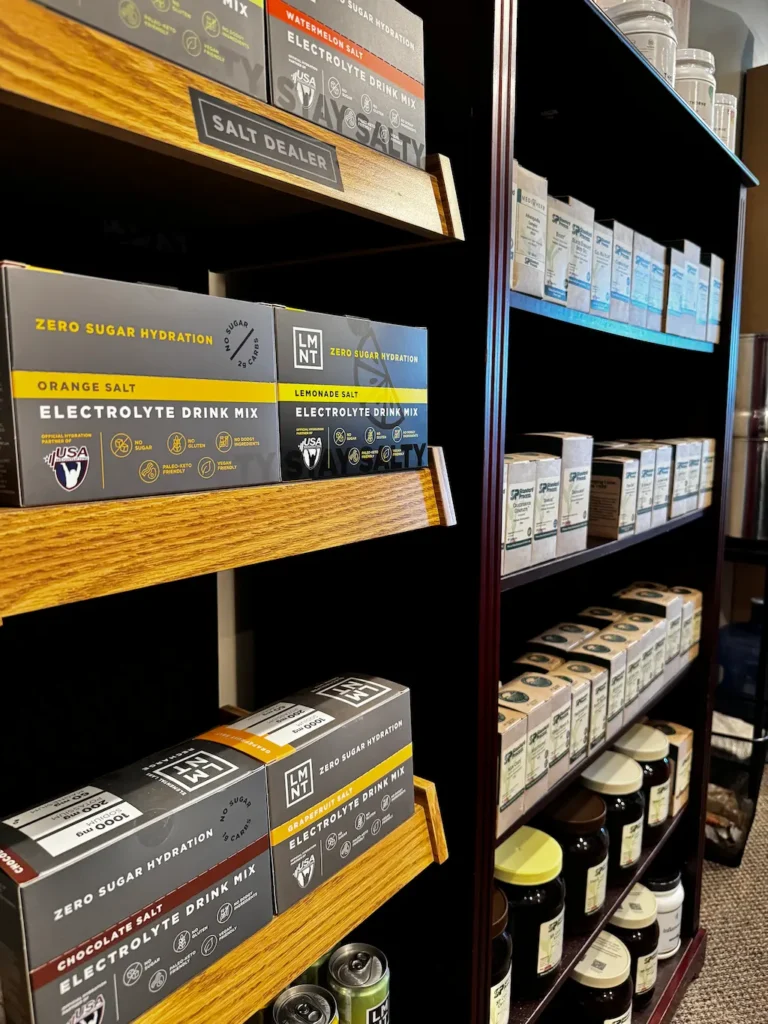 A store display featuring boxes of LMNT Zero Sugar Hydration electrolyte drink mixes in various flavors like Orange Salt, Lemonade Salt, and Watermelon Salt, on wooden and dark shelves.