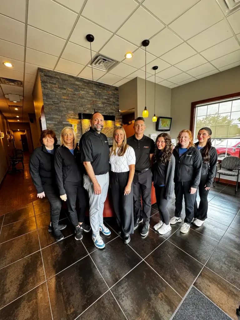 Eight people, four men and four women, smiling and standing in a reception area with a stone-faced wall and dark tiled floor.