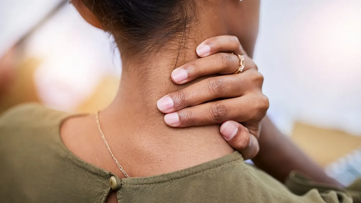 Close-up of a person's hand grasping the back of their neck, wearing a green top and a gold ring.