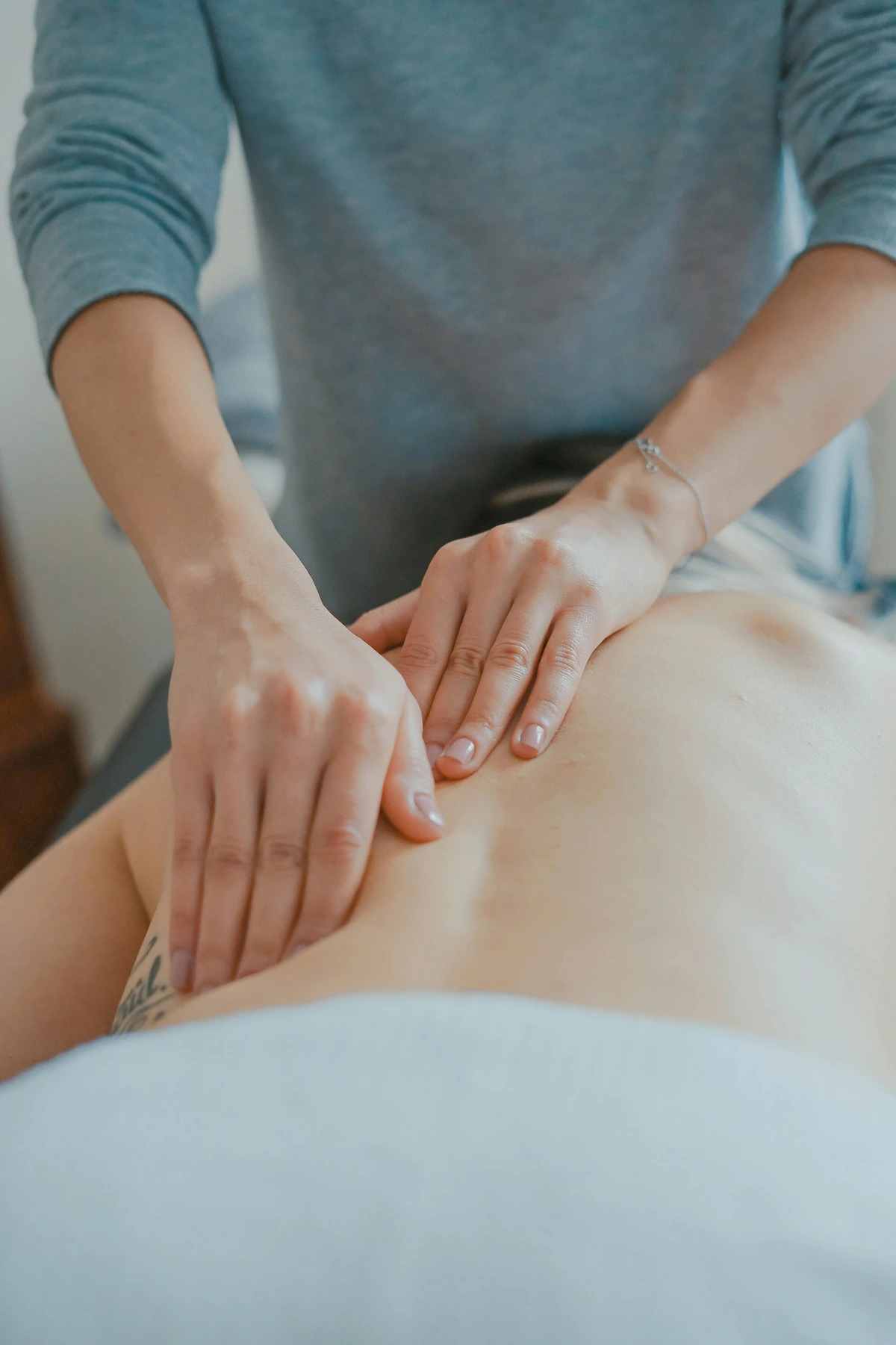 Close-up of a masseur's hands giving a back massage to a person lying on a white sheet.
